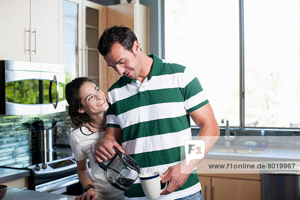 Junges Paar das Kaffee aus der Kanne in die Küche gießt lächelnd