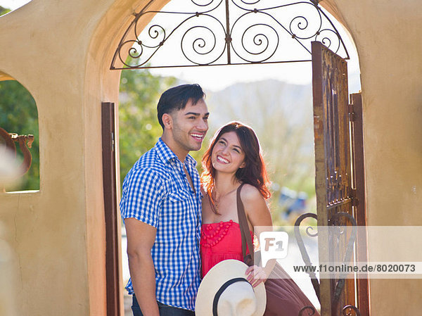 Junges Paar lächelt gemeinsam am Eingang der Villa