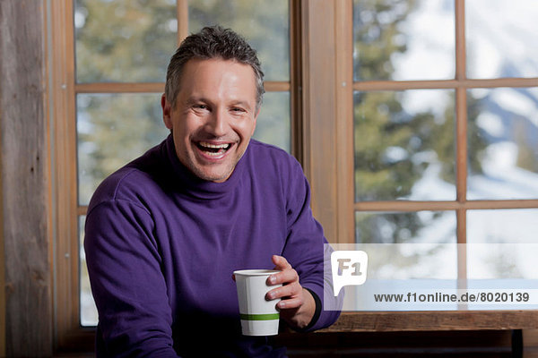Mature man holding hot drink indoors  laughing