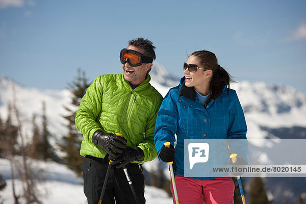 Junge Frau und reifer Mann in Skibekleidung mit Skistöcken