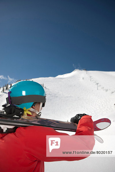 Young woman in skiwear holding skis over shoulder at the bottom of ski slope