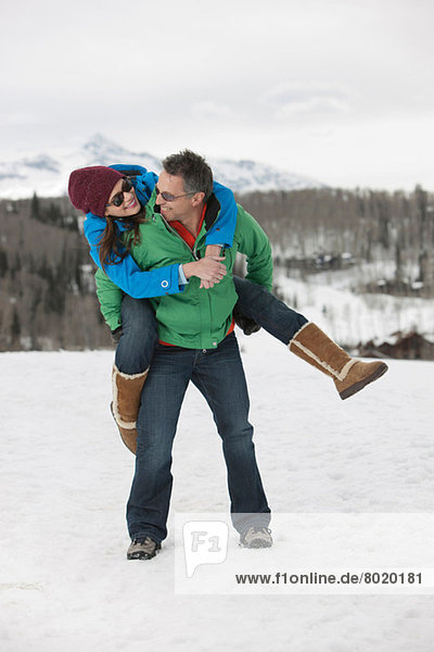 Mature man carrying young woman on back in snow