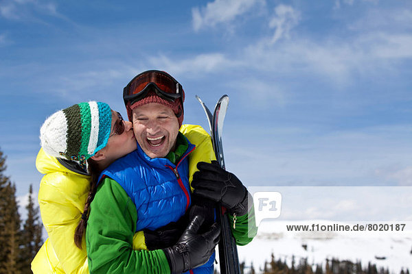 Junge Frau in Skibekleidung küssend reifer Mann mit Skiern