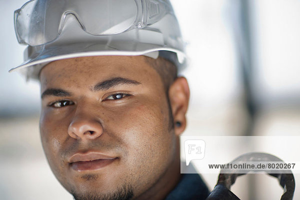 Junger Bauarbeiter mit Schutzhelm und Halteschlüssel  lächelnd