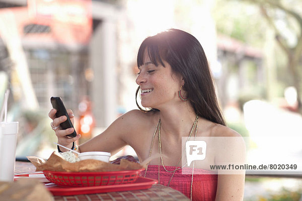 Junge Frau mit Handy im Outdoor-Café  lächelnd