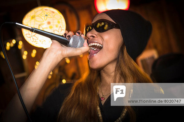 Woman wearing hat and sunglasses singing in microphone