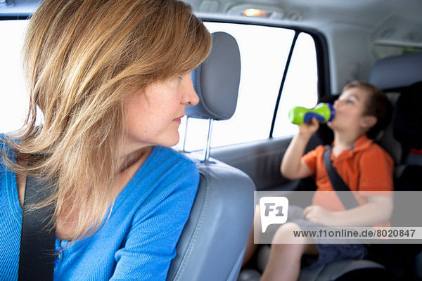 Mutter sieht zu  wie der Junge aus der Flasche auf dem Rücksitz des Autos trinkt.