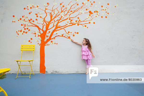 Mädchen zeigt auf Orangenbaumwand an der Wand