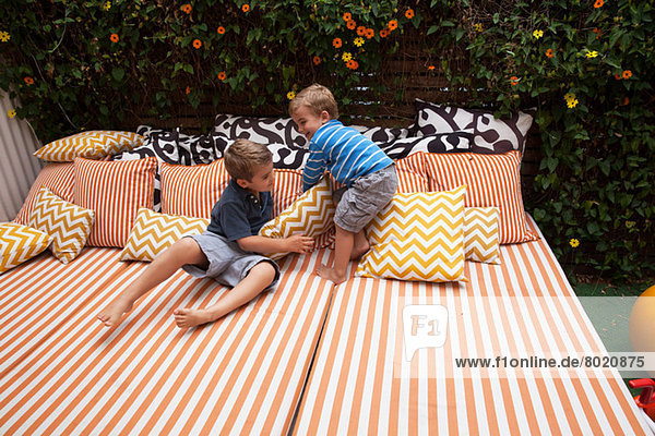 Zwei Jungen  die auf Gartenmöbeln mit Kissen spielen.