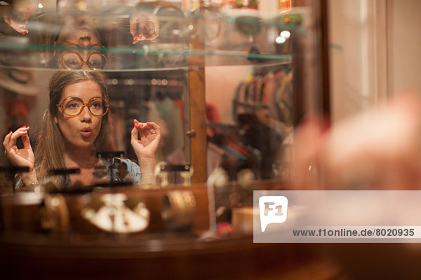 Junge Frau probiert Brille an und zieht Gesichter im Vintage-Shop