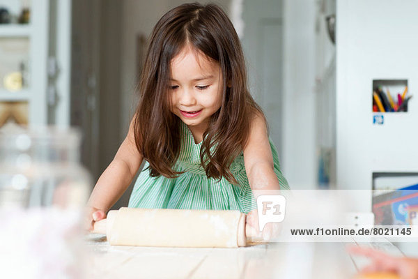 Young girl rolling out pastry on kitchen counter