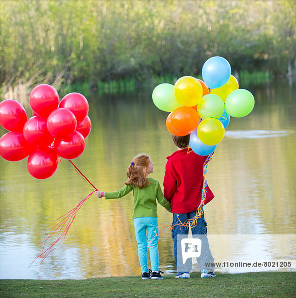 Bruder und Schwester halten Luftballons im Park.