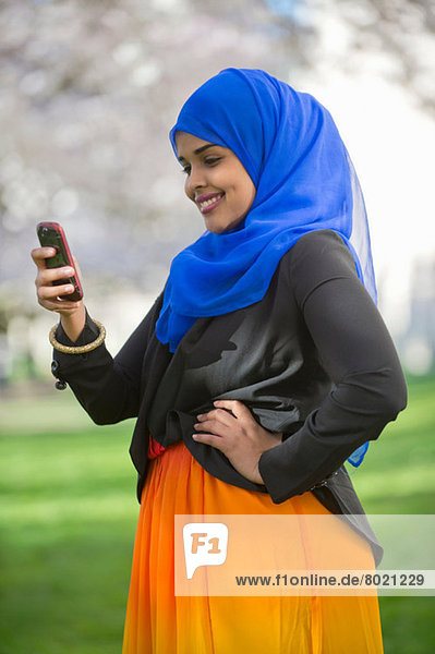 Porträt einer jungen Frau im Park mit Blick auf ihr Handy