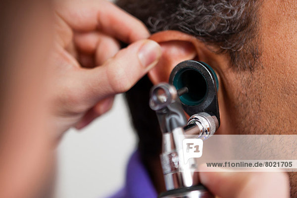 Mid adult doctor using otoscope on patient