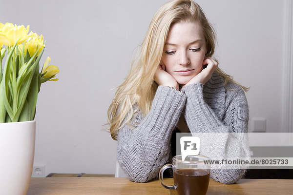 Junge Frau sitzt nachdenklich vor ihrer Teetasse