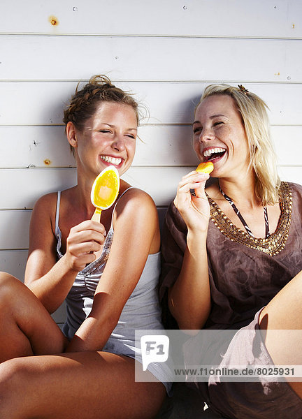 Portrait of two beautiful women eating ice-cream on the beach.