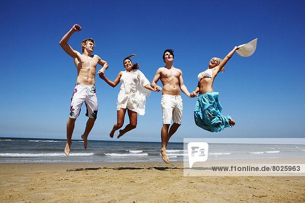 Two young man and two young women are jumping on the beach.