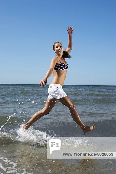 Portrait of a young beautiful woman running through the water on the beach.