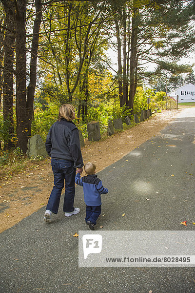 A two-year old boy walks on a paved road in a park holding his grandmother's hand Willimantic connecticut united states of america