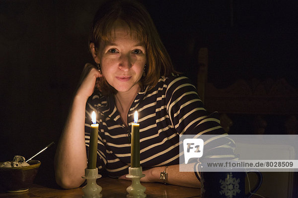 A woman sitting at a table in a dark room with a coffee cup and a bowl of ice cream being illuminated by two candles in front of her Willimantic connecticut united states of america