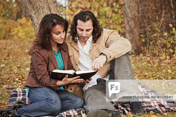 Married couple reading a bible in a park in autumn Edmonton alberta canada