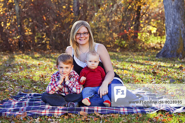 Portrait of a mother with her young son and baby daughter in a park in autumn Edmonton alberta canada