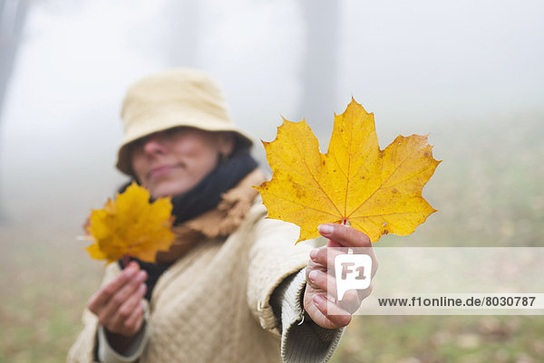 A woman holding a large bright yellow maple leaf in the fog Bellinzona ticino switzerland