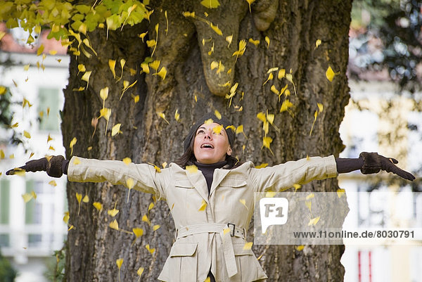 A woman stands in front of a tree with arms outstretched as yellow leaves shower down on her Locarno ticino switzerland