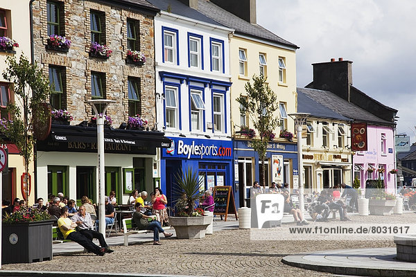 People sitting outside colourful retail buildings Clifden county galway ireland