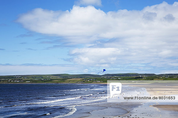 A busy beach with people surfing swimming and flying kites Lahinch county clare ireland