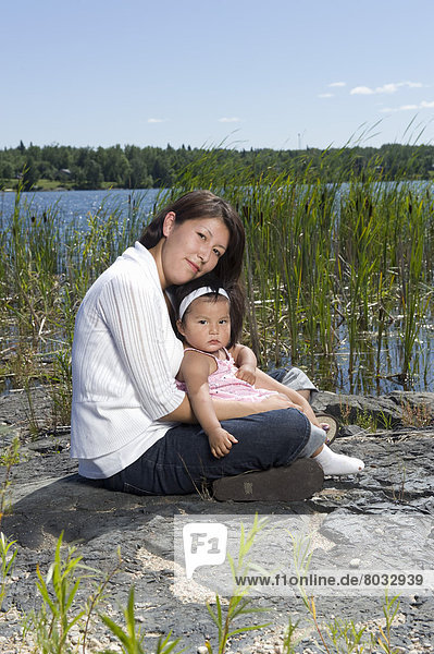 Felsbrocken  sitzend  nebeneinander  neben  Seite an Seite  Fischschwarm  See  1  Tochter  Schilf  Ethnisches Erscheinungsbild  Mutter - Mensch  Kanada  alt  Ontario  Jahr