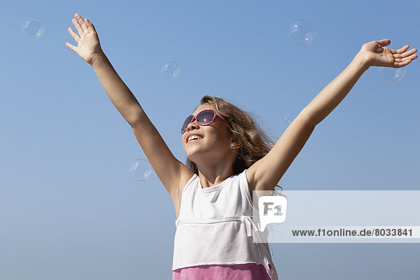 Young smiling girl in sunglasses reaching for bubbles against a clear blue sky Whitby ontario canada