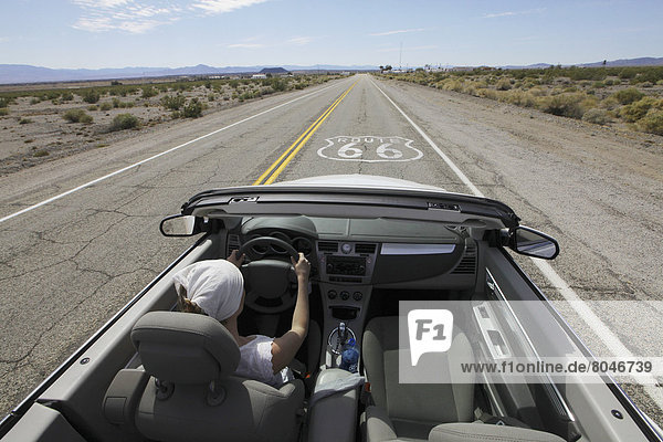 USA  Young woman driving her convertible car through desert along Route 66  California