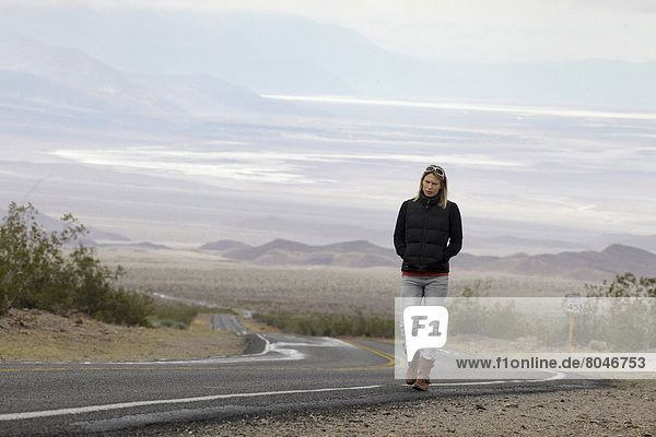 USA  Nevada border  California  Route 374  Death Valley National Park  Highway 374  Young woman walking on deserted road in desert