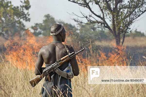 Ethiopia  Southern Nations Nationalities and Peoples' Region  South Omo  Rear view of Mursi tribal man looking at controlled fire on savanah  Southern Mursiland
