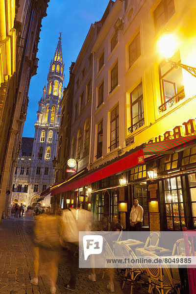 People walking down side street in front of restaurant with Town Hall behind in Grand Place at dusk  Brussels  Belgium