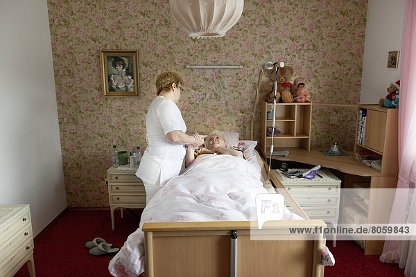 Altenpflegerin spricht mit alter Frau im Bett