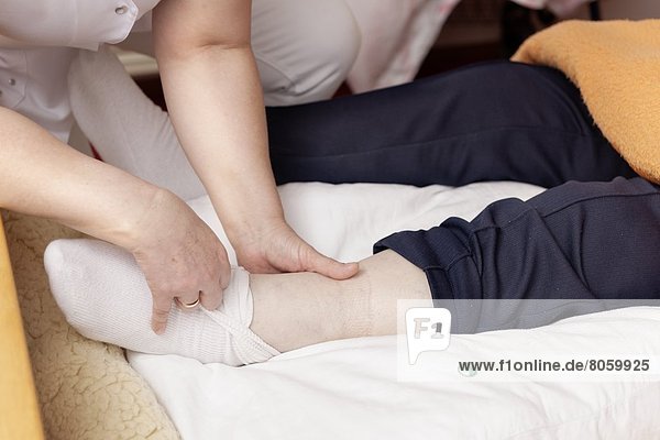 Altenpflegerin bandagiert Bein einer alter Frau