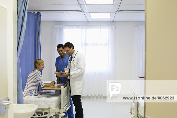 Arzt und Krankenschwester im Gespräch mit dem Patienten im Krankenhauszimmer