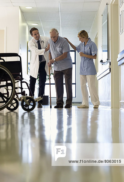 Arzt und Krankenschwester helfen älteren Patienten beim Gehen im Krankenhaus