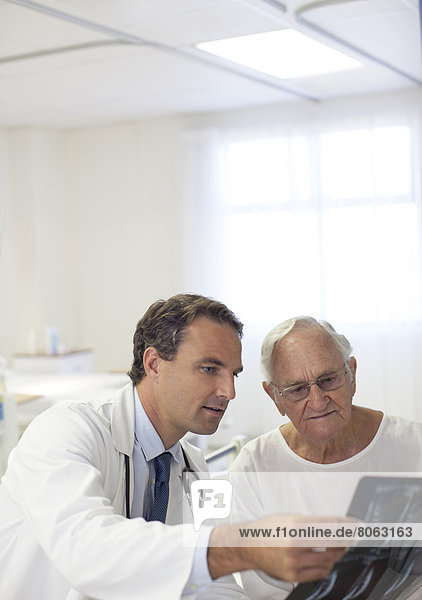 Arzt zeigt älteren Patienten Röntgenaufnahmen im Krankenhauszimmer