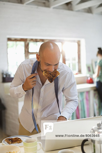 Businessman eating breakfast and using laptop