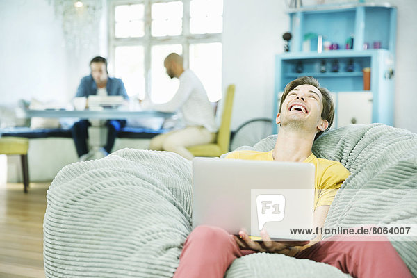 Laughing man using laptop in beanbag chair