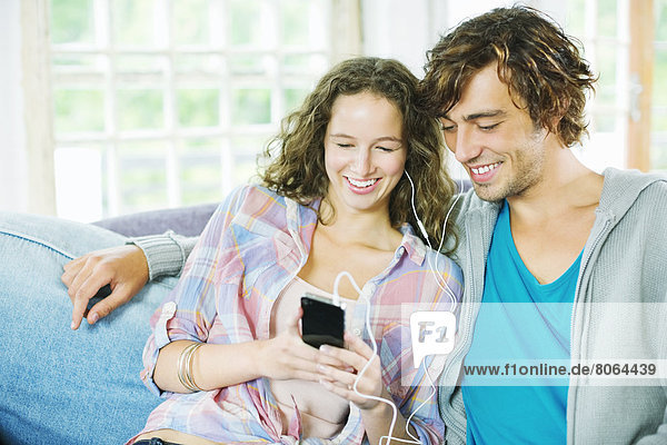 Couple listening to earphones together on sofa