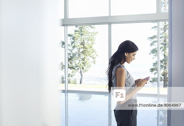 Businesswoman using cell phone at window