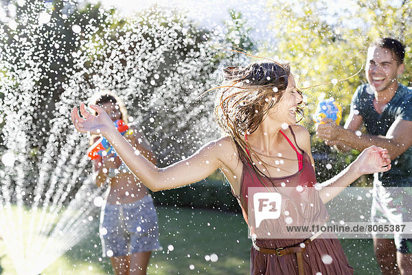 Friends playing with water guns in sprinkler