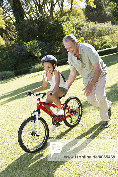 Older man teaching granddaughter to ride bicycle