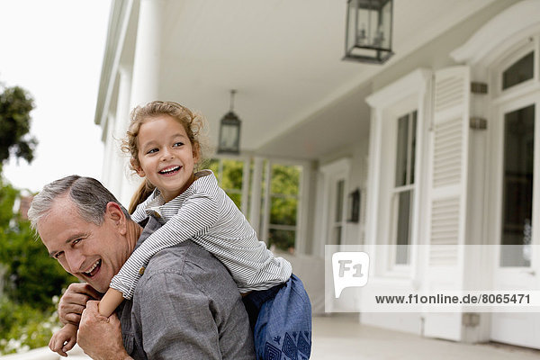 Older man carrying granddaughter piggy back on porch