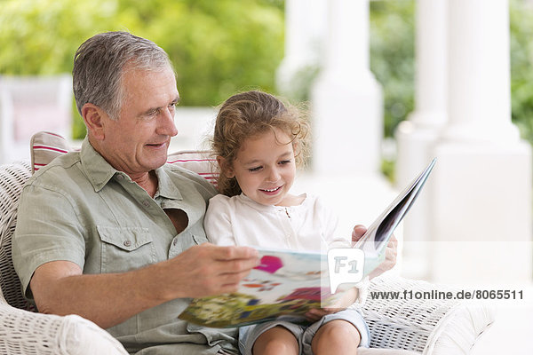 Older man reading to granddaughter on porch