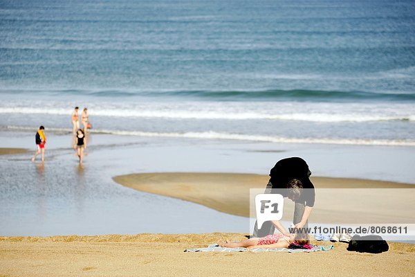 eincremen  verteilen  Strand  Menschlicher Vater  klein  Creme  Salbe  Lotion  sonnenbaden  sonnen  groß  großes  großer  große  großen  auftragen  Biarritz
